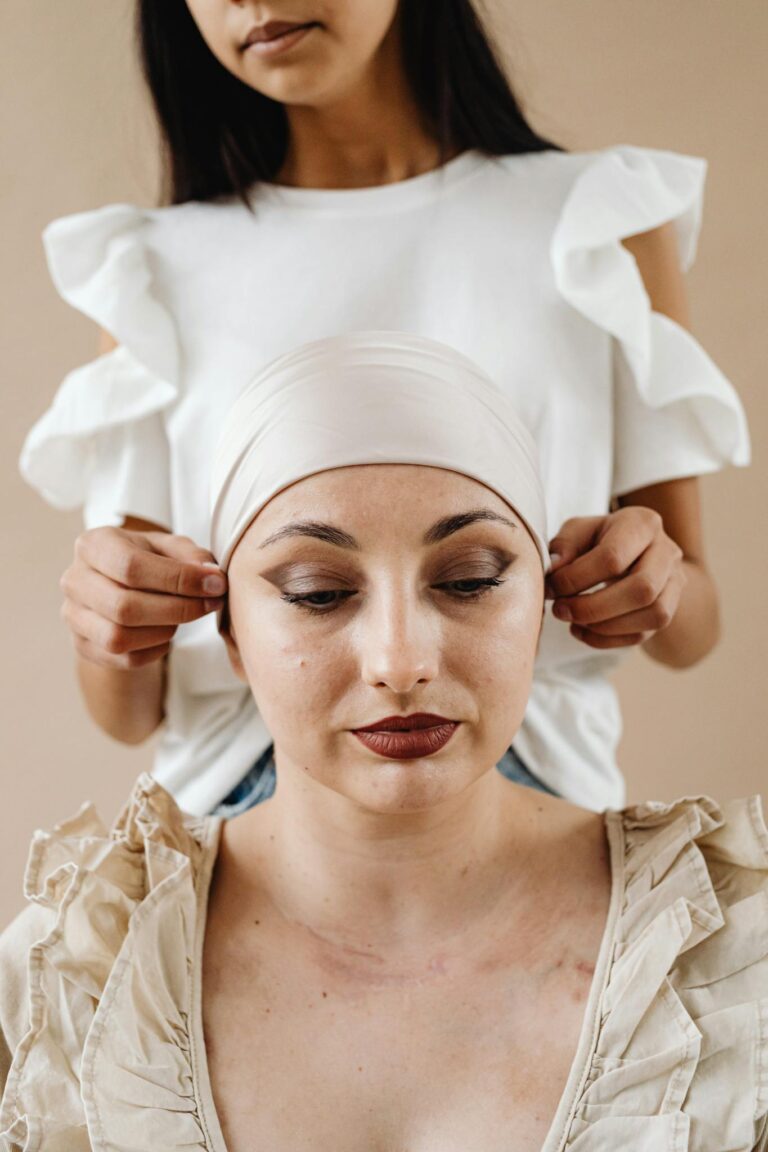 A woman assists her friend with a headscarf, symbolizing support during cancer treatment.