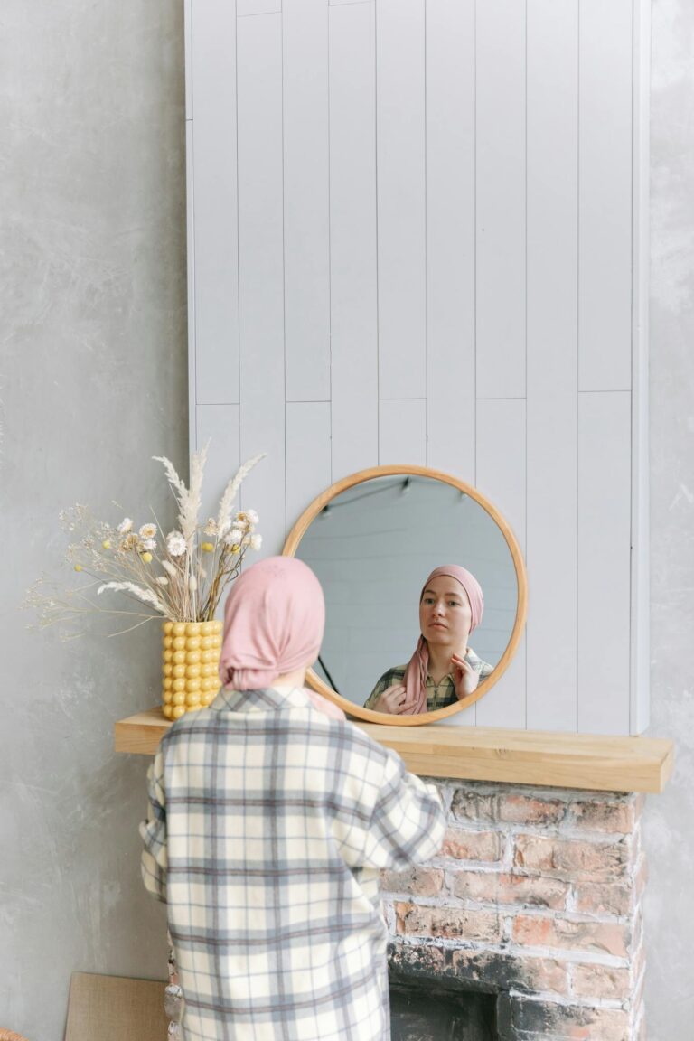 A woman with a headscarf reflects in a mirror, symbolizing cancer survival and awareness.