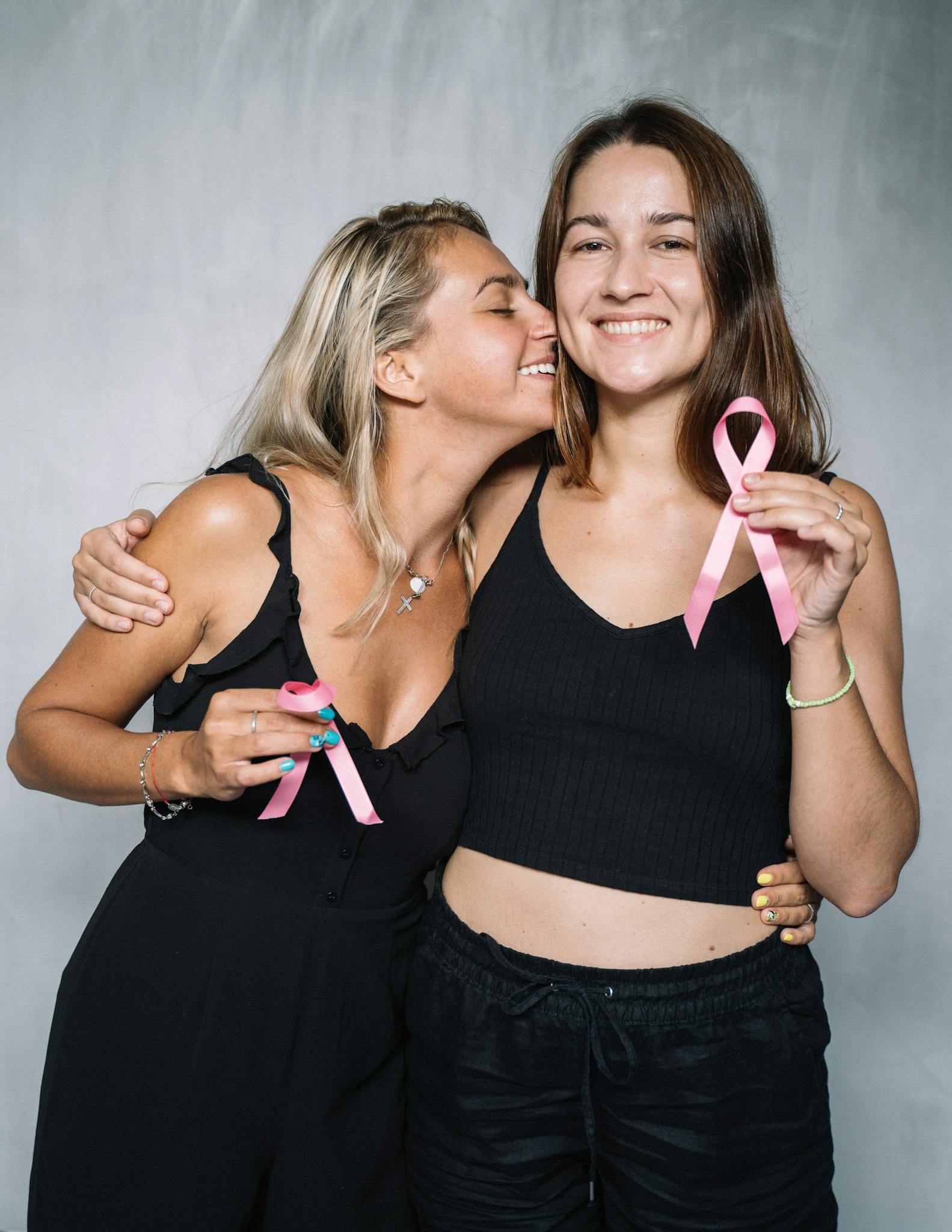 Two women celebrating breast cancer awareness with pink ribbons and smiles.